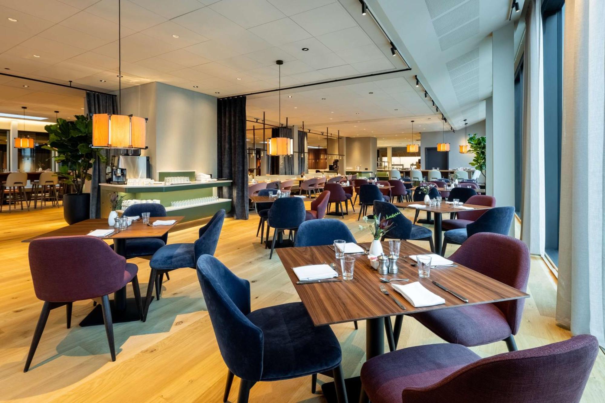 Nh Collection Copenhagen Hotel Luaran gambar The photo showcases a modern restaurant interior with a spacious and elegant design. It features wooden flooring and a combination of light and dark furnishings. There are several tables set for dining, each with utensils and glasses. The chairs come